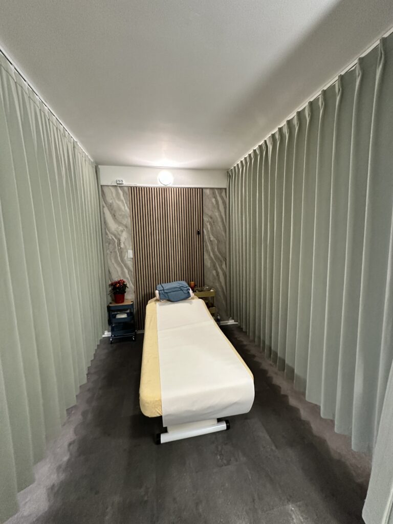 Ruhige Behandlungskabine im SanBao – Zentrum für Balance Ruhig gestaltete Behandlungskabine mit Massageliege und umlaufenden Vorhängen im SanBao – Zentrum für Balance in Wien